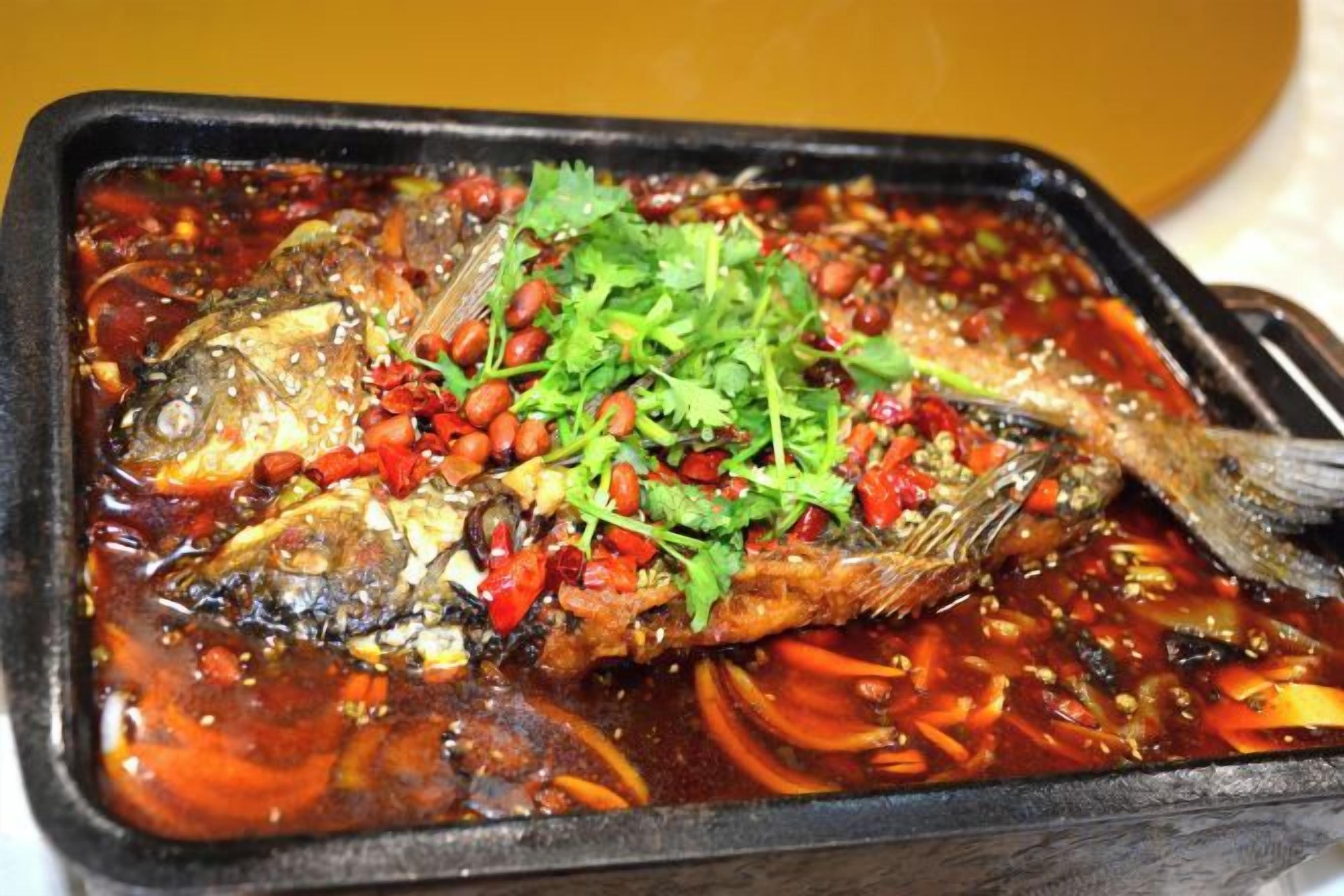 A dish with fish, red chili, and herbs in a black container.
