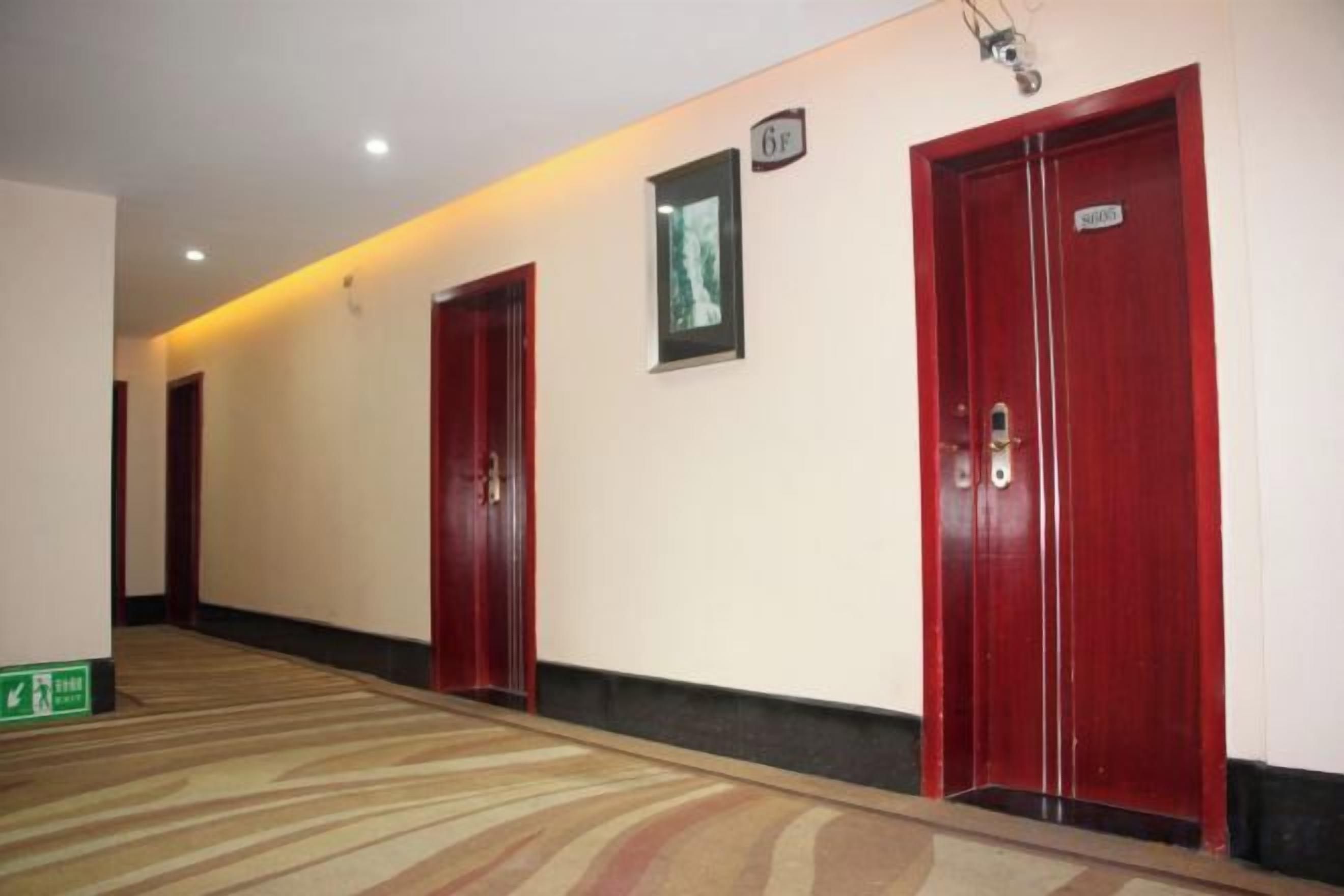 A hotel corridor with red doors, a carpeted floor, and a green exit sign.