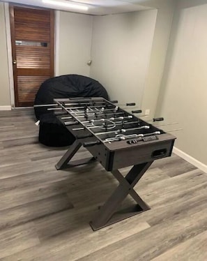 Une table de baby-foot dans une pièce dont le sol est recouvert de parquet, avec une porte visible au fond.