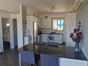 A modern kitchen with a central island, a built-in washing machine, and a dining area with a glass table and chairs.