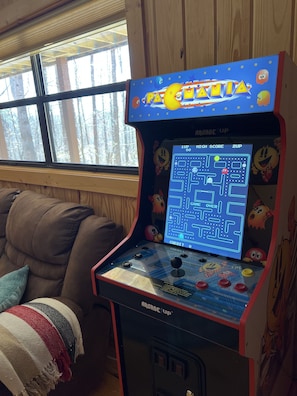 Ein Retro-Arcade-Automat mit einem Labyrinthspiel, in einem Raum mit Fenster und Sofa.