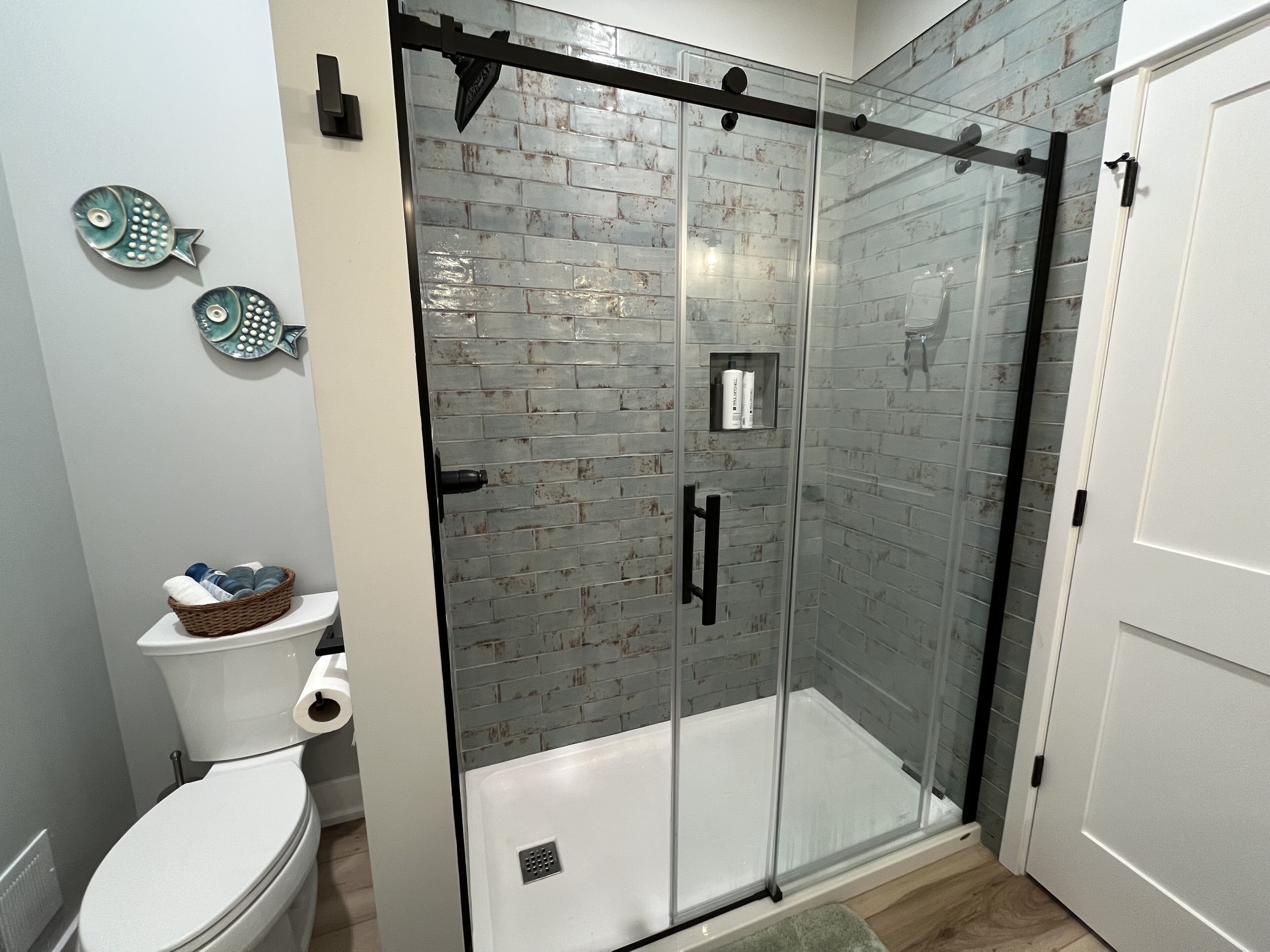 A modern bathroom with a glass-enclosed shower, a toilet, and decorative fish wall art.