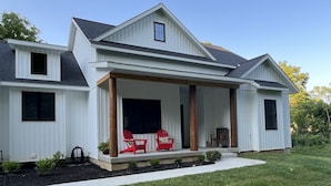 A modern two-story house with a covered porch, two red Adirondack chairs, and a small garden area. - Coastal Farmhouse-located in "The Best Coastal Small Town in America" -USA Today (Saugatuck)