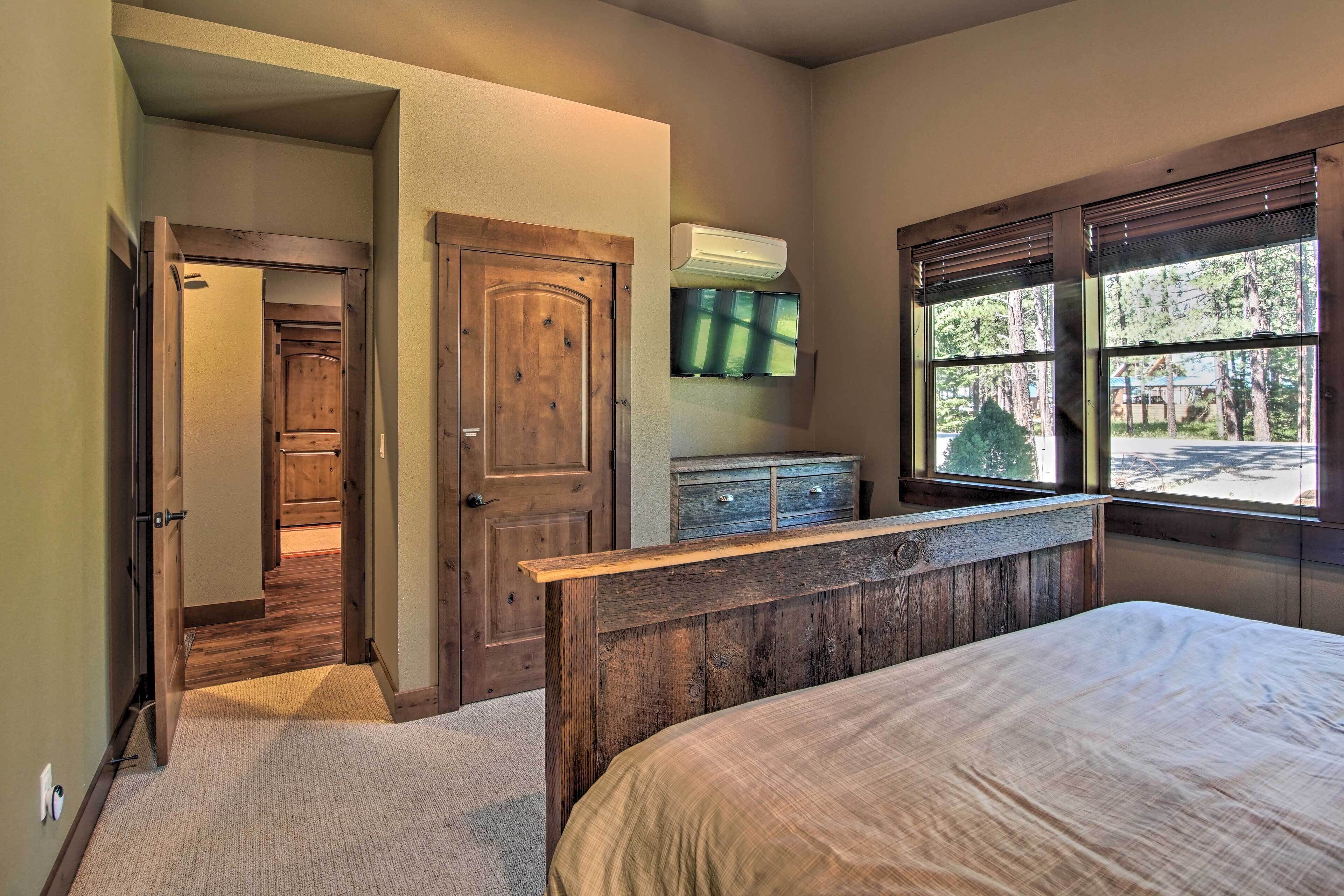 Een slaapkamer met een houten hoofdeinde, een bed, een dressoir en een raam met uitzicht op bomen.