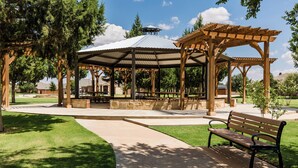 A gazebo with a metal roof and wooden beams, surrounded by a well-maintained lawn and trees. - The ultimate resort ranch style pool home on nearly a half acre! (Lubbock)