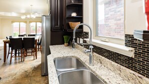 A kitchen with a double sink, dark wooden cabinets, a stainless steel refrigerator, and a window overlooking a brick wall. - The ultimate resort ranch style pool home on nearly a half acre! (Lubbock)