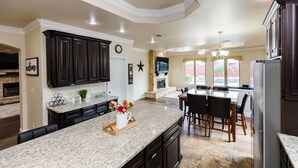 A spacious kitchen with dark cabinetry, a granite countertop, and a large island with seating. - The ultimate resort ranch style pool home on nearly a half acre! (Lubbock)