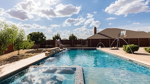 A swimming pool with a slide, surrounded by a wooden fence, trees, and a building with a chimney. - The ultimate resort ranch style pool home on nearly a half acre! (Lubbock)