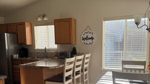 A kitchen with wooden cabinets, a central island with chairs, a welcome sign, and a large window.