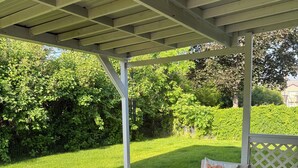 An outdoor patio area with wicker furniture, a fire pit, and a view of a well-maintained lawn and trees.