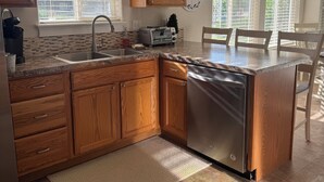 A kitchen with wooden cabinets, a stainless steel dishwasher, a built-in oven, and a large window with blinds.