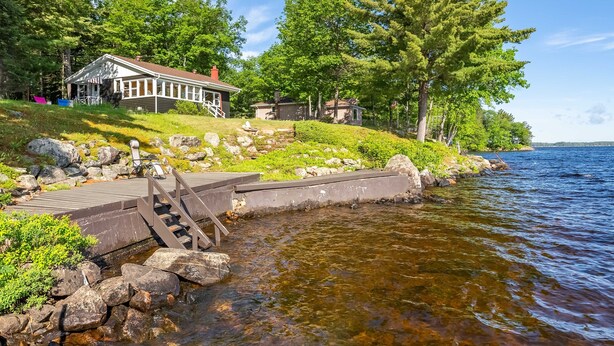 A lakeside cabin with a dock, surrounded by greenery and trees.