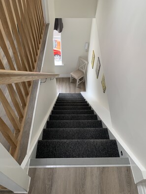 Stairs lead to a cozy upper floor with a chair at the top, framed pictures on the wall, and a window for natural light.