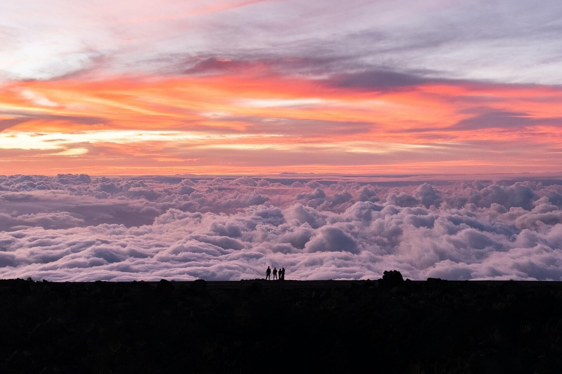 Panorama di un paesaggio montuoso con un'ampia copertura nuvolosa in basso e un tramonto colorato sopra.
