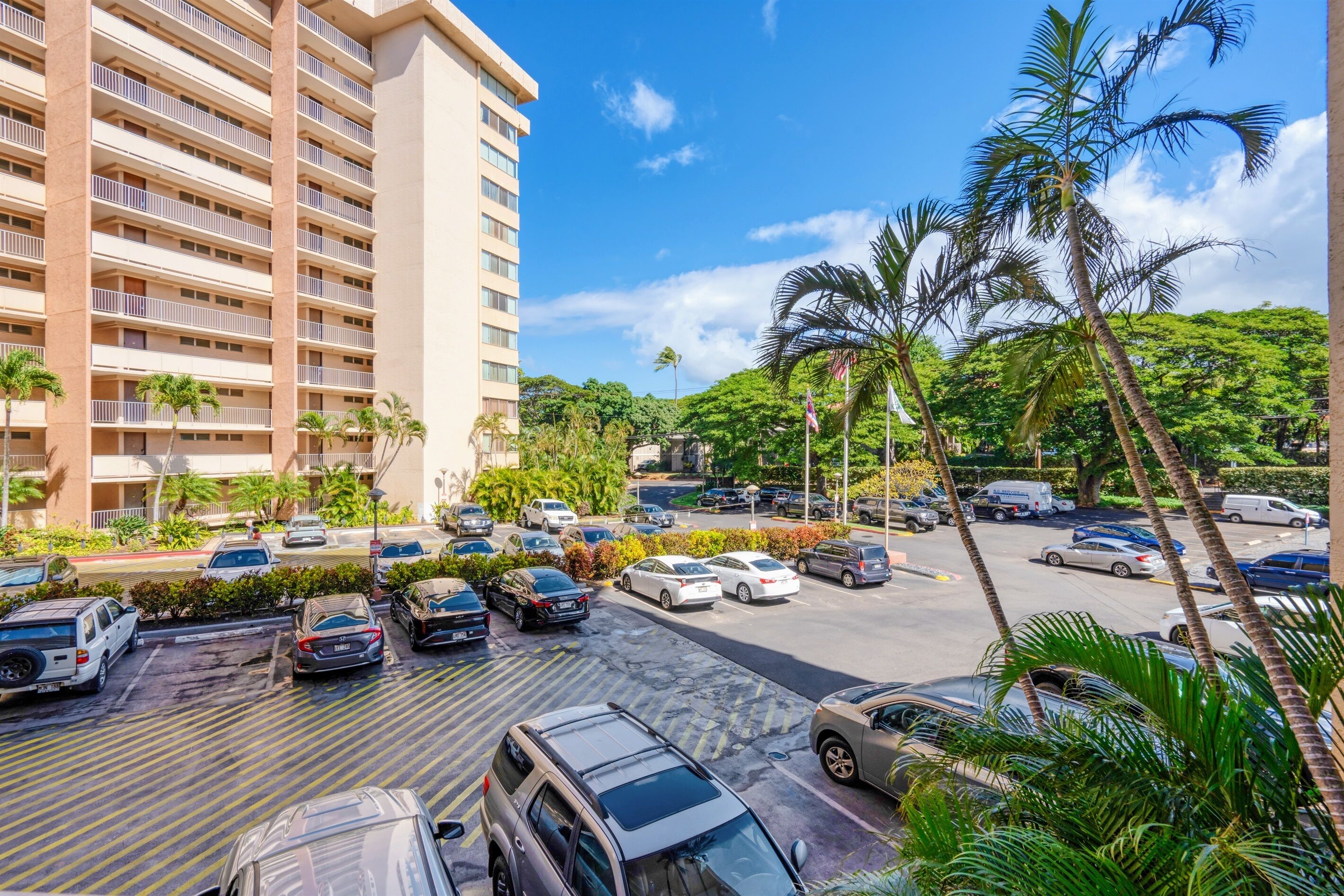 A multi-story hotel with a parking lot filled with cars, surrounded by palm trees and greenery.