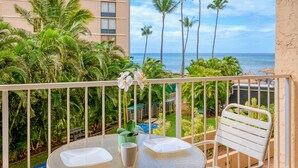 A balcony with a table, chairs, and a view of the ocean and palm trees.