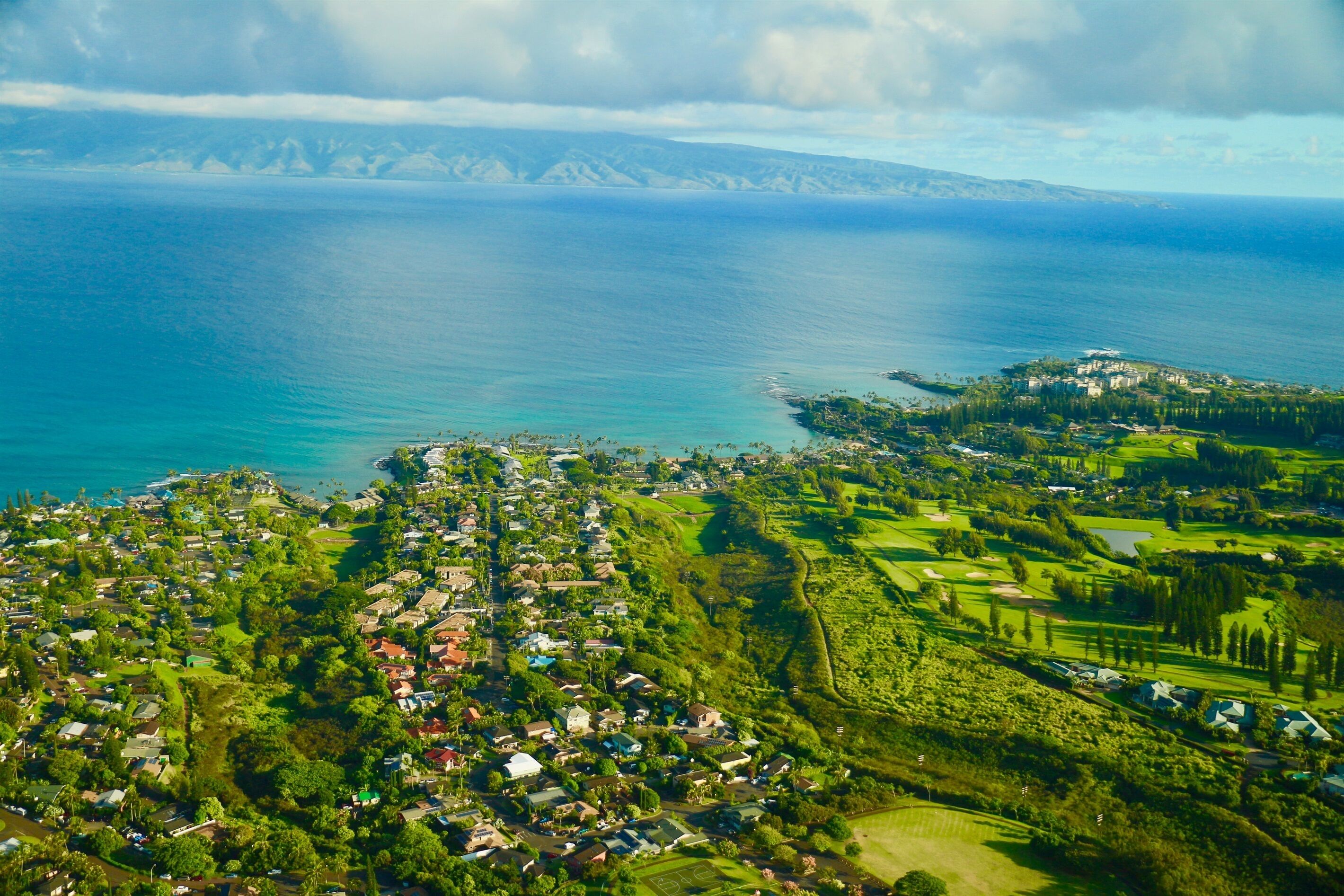 An aerial view of a coastal town with residential areas, golf courses, and a large body of water.