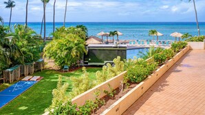 A resort pool area with lounge chairs, palm trees, and a view of the ocean.
