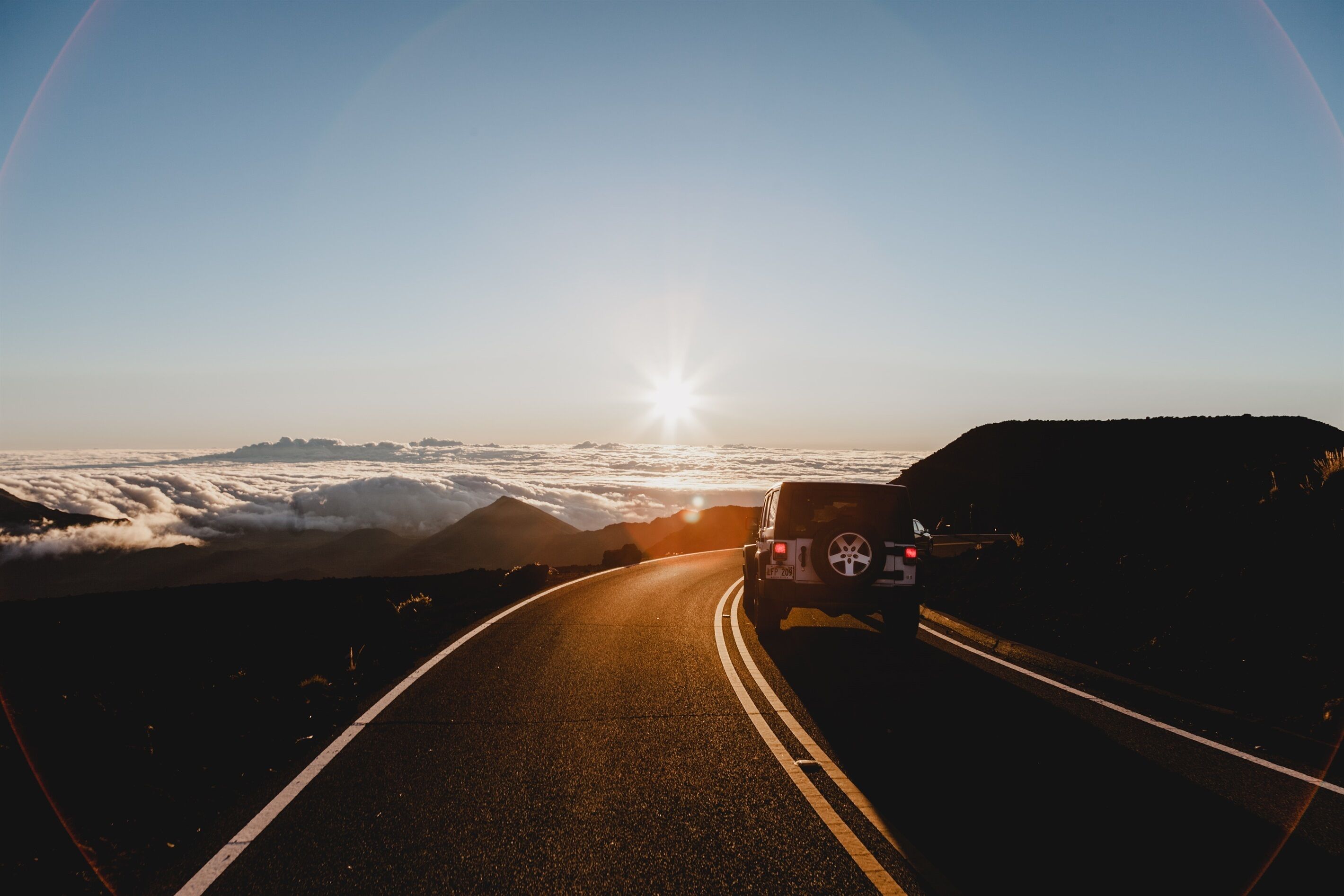 Un véhicule sur une route, avec un ciel dégagé et le soleil se couchant ou se levant.