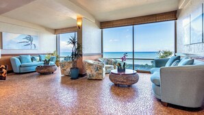 A spacious living area with a large window overlooking the ocean, furnished with sofas and a coffee table.