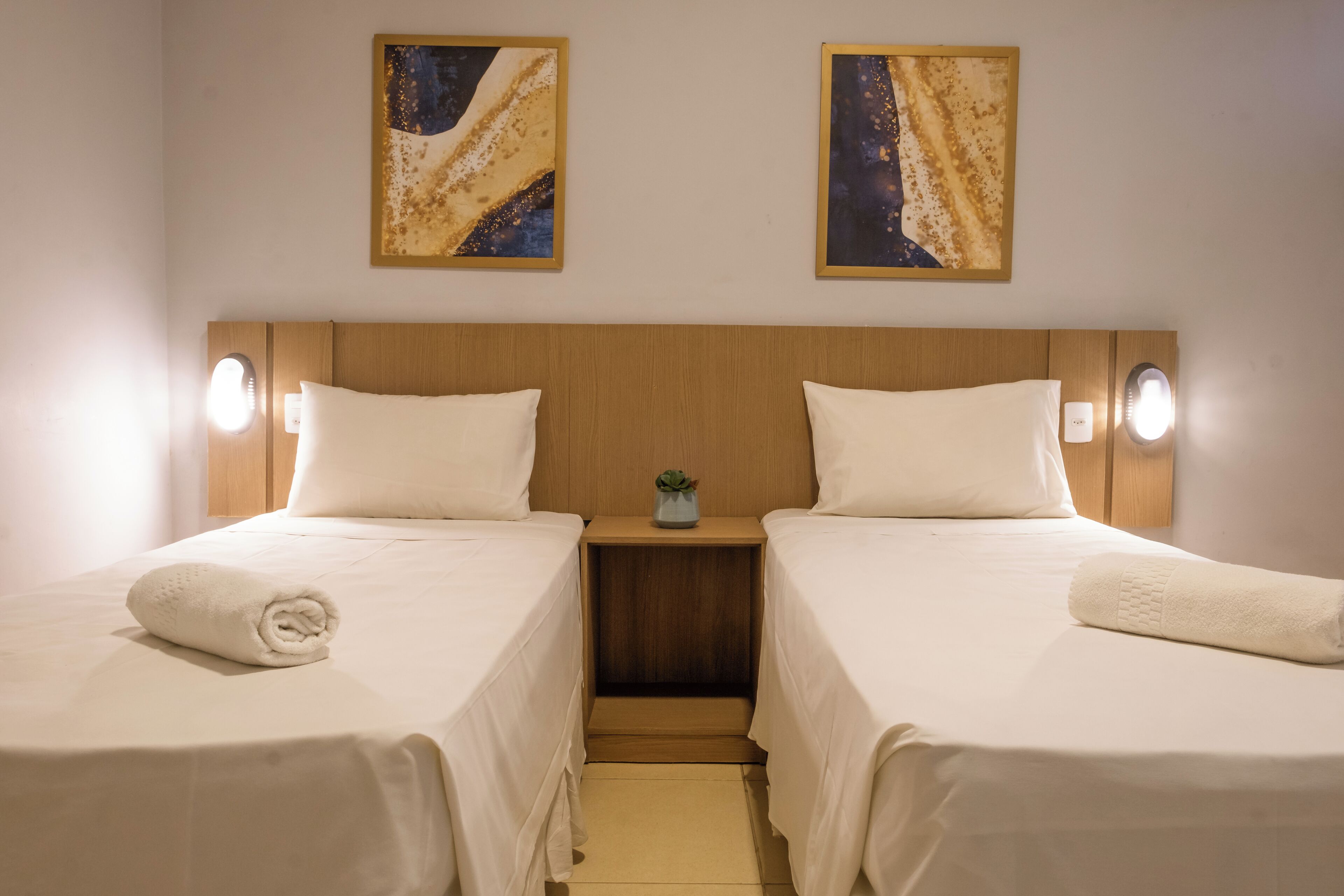 Una habitación de hotel con dos camas, cabecero de madera y obras de arte en las paredes.