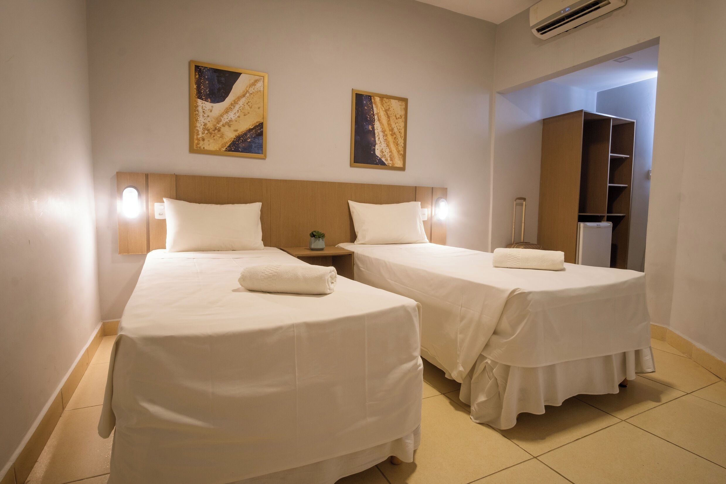 A hotel room with two single beds, a nightstand, a small table, and a wardrobe.