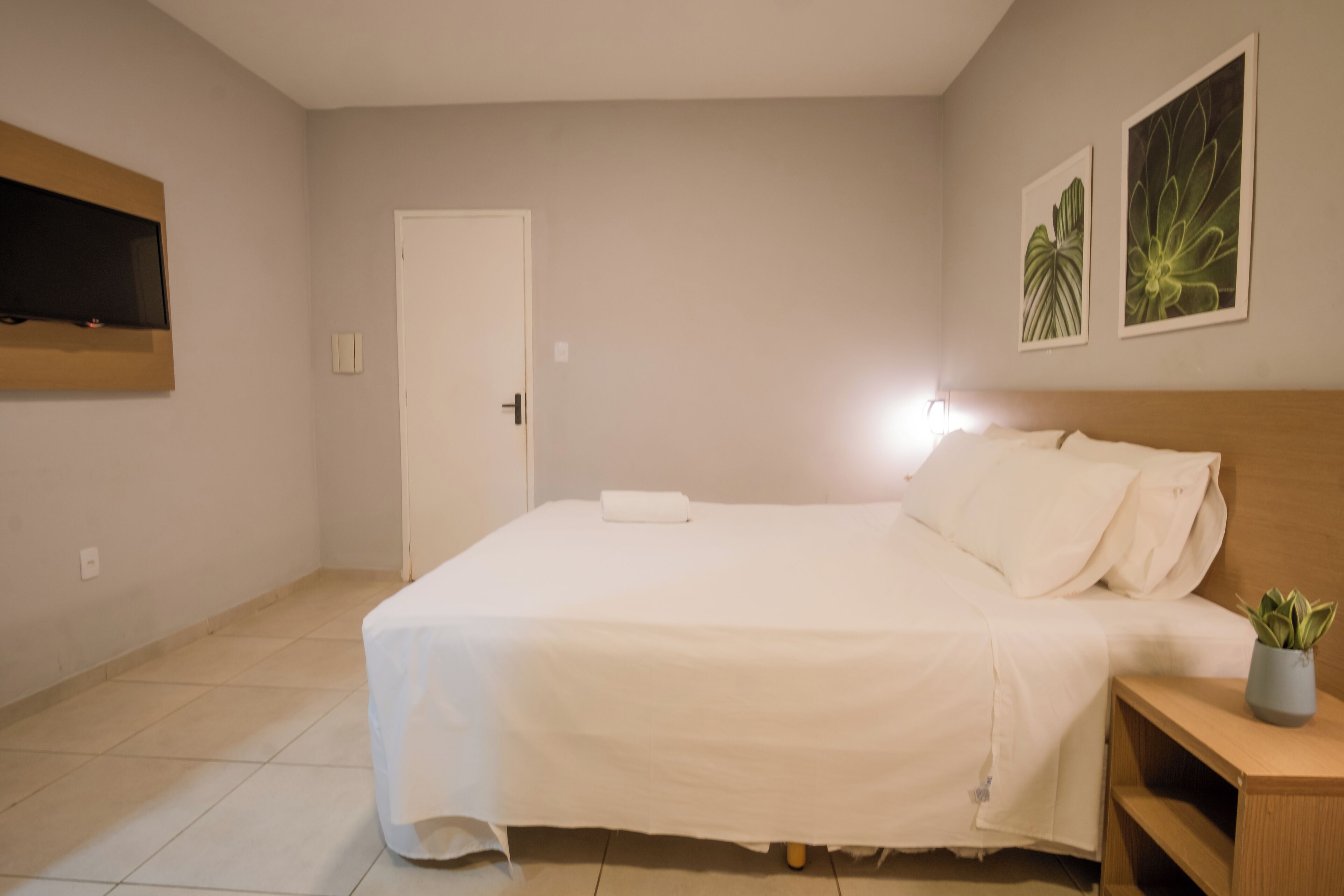 A bedroom with a bed, a TV mounted on the wall, and two framed pictures.
