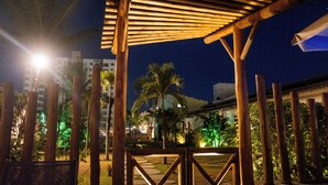 An outdoor area with a wooden pergola, palm trees, and a pathway leading to a building. - Marezzi Hotel (Aracaju)