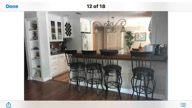 A kitchen with white cabinets, a bar area with four stools, and a chandelier.