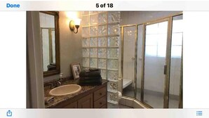 A bathroom with a glass shower enclosure, a sink with a vanity, and a wall-mounted light fixture.