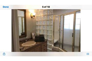 Une salle de bain avec une douche à parois de verre, un lavabo avec un meuble-vasque et un luminaire fixé au mur.