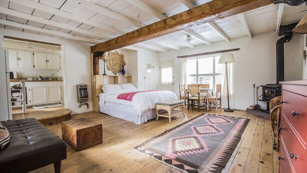 A spacious room with a large bed, wooden beams, a dining area, and a kitchen. - Writer’s Farm Cabin: Hot Tub Saunas Farm Animals (San Cristobal)