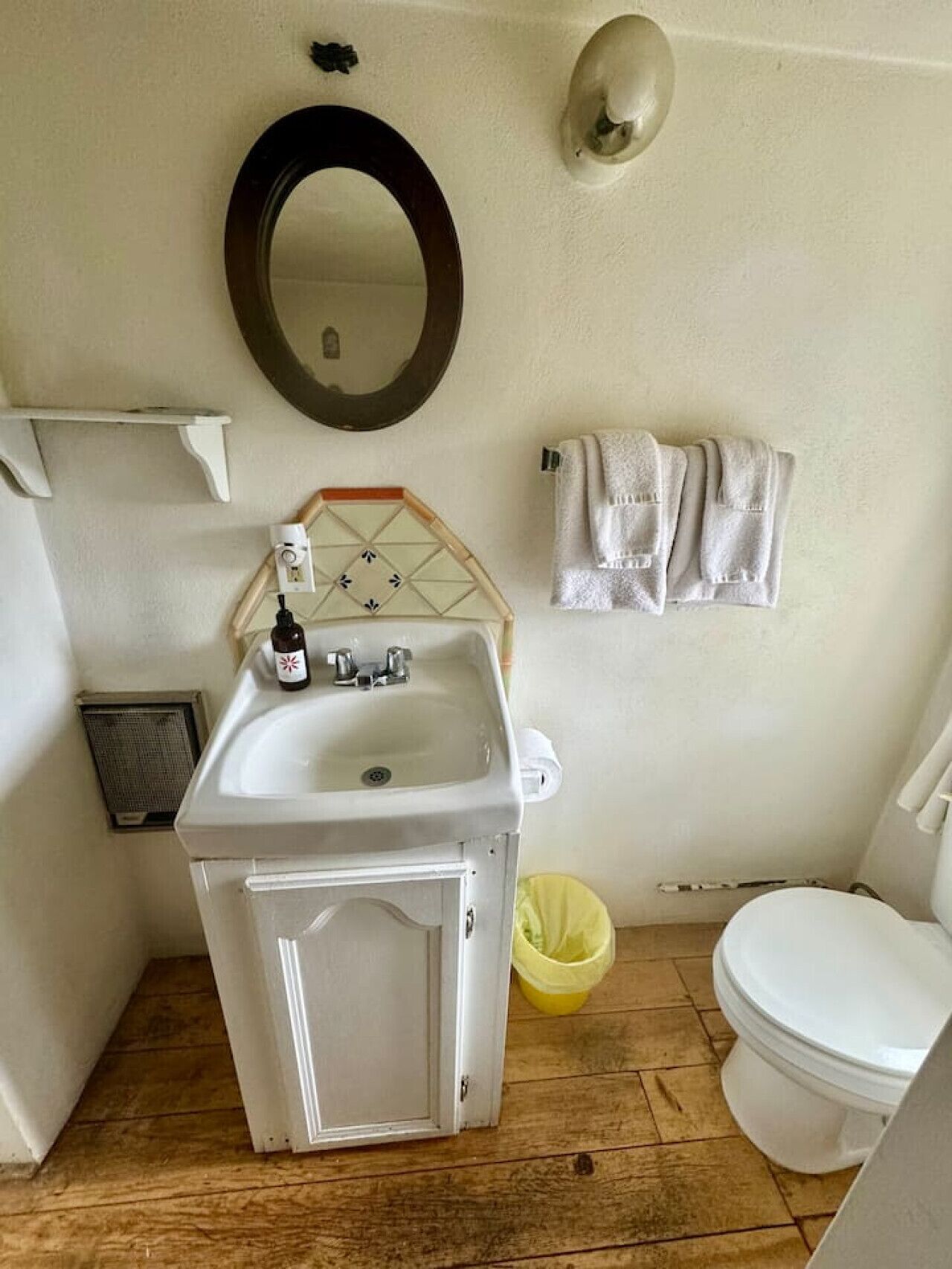 A bathroom with a white sink, mirror, and toilet. There is a yellow bucket and a white towel rack.