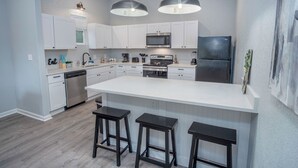 A modern kitchen with white cabinets, a central island with stools, stainless steel appliances, and pendant lighting. - Cozy and Lovely 2BR 2BA Apt#a Near Lively Downtown (San Antonio)