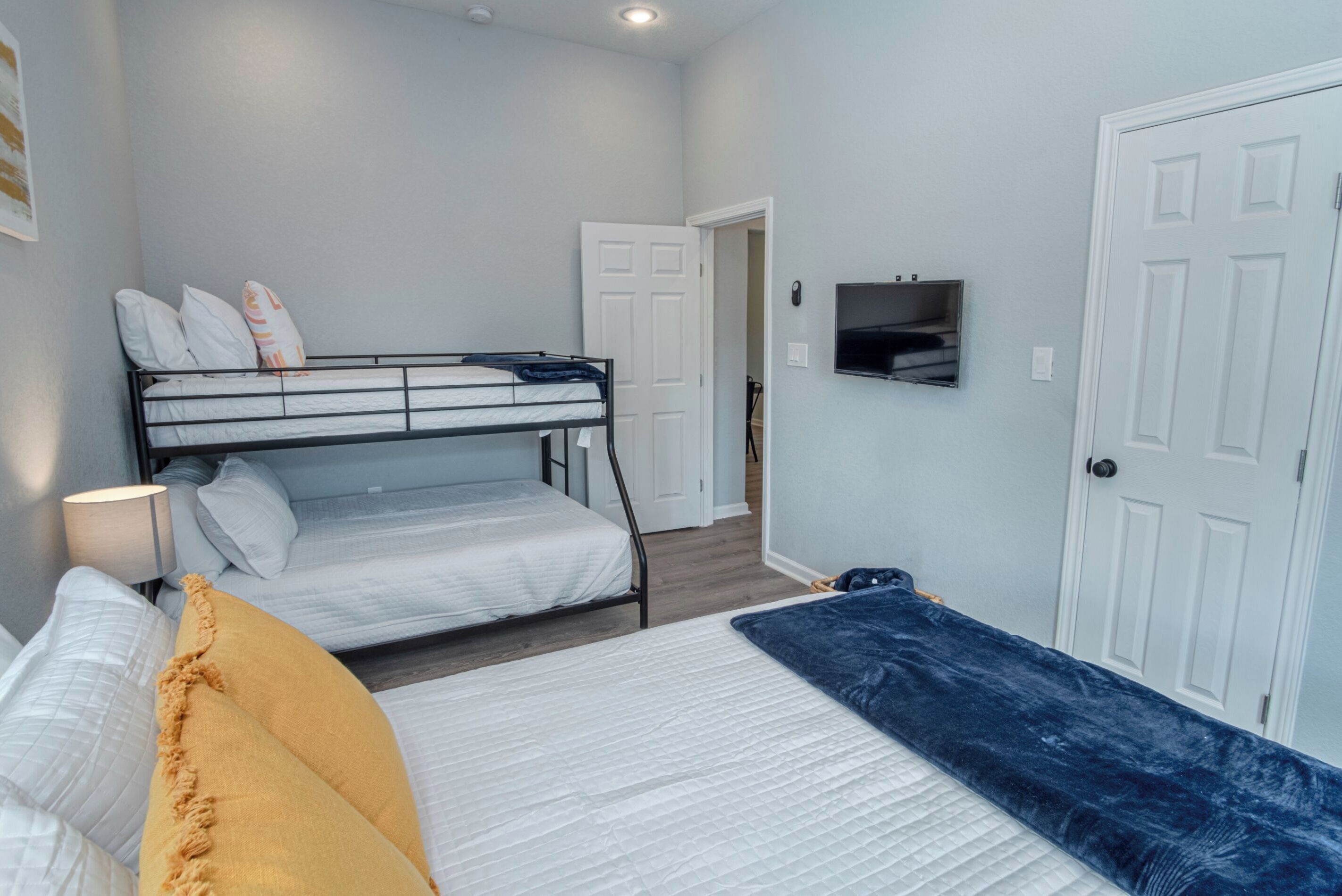 Una habitación con una cama litera, una cama individual, un televisor montado en la pared y una puerta.
