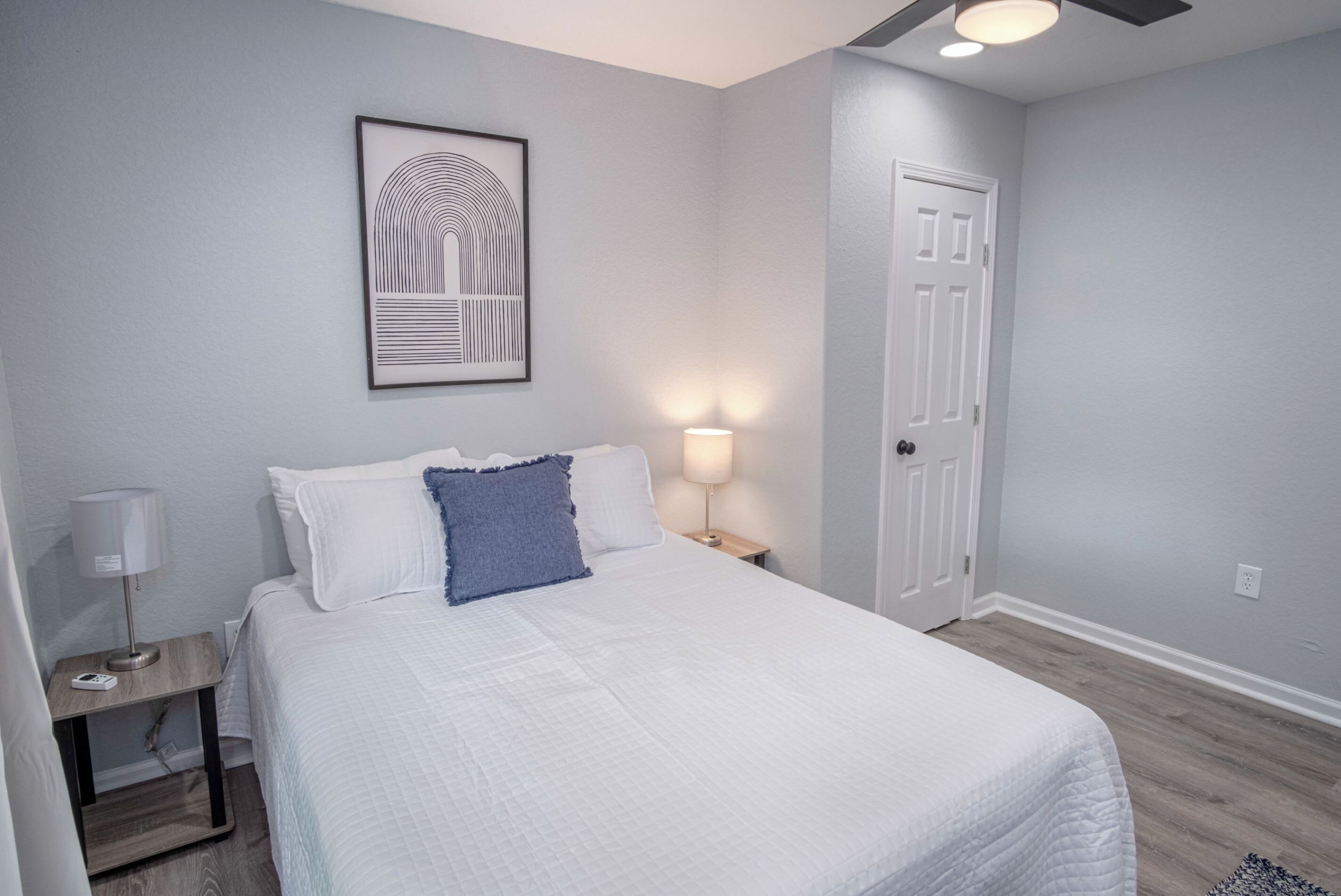 A bedroom with a bed, a nightstand, a lamp, a door, and a ceiling fan.