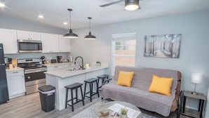 A modern kitchen with white cabinets, a central island, and a dining area with a sofa and stools. - Cozy and Lovely 2BR 1BA Apt#b Near Lively Downtown (San Antonio)