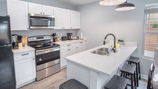 A modern kitchen with white cabinets, stainless steel appliances, and a central island with stools. - Cozy and Lovely 2BR 1BA Apt#b Near Lively Downtown (San Antonio)