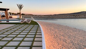 Ett poolområde med en sandstrand och utsikt över vattnet.