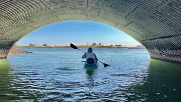 A kayaker under a bridge with calm water and a clear sky.