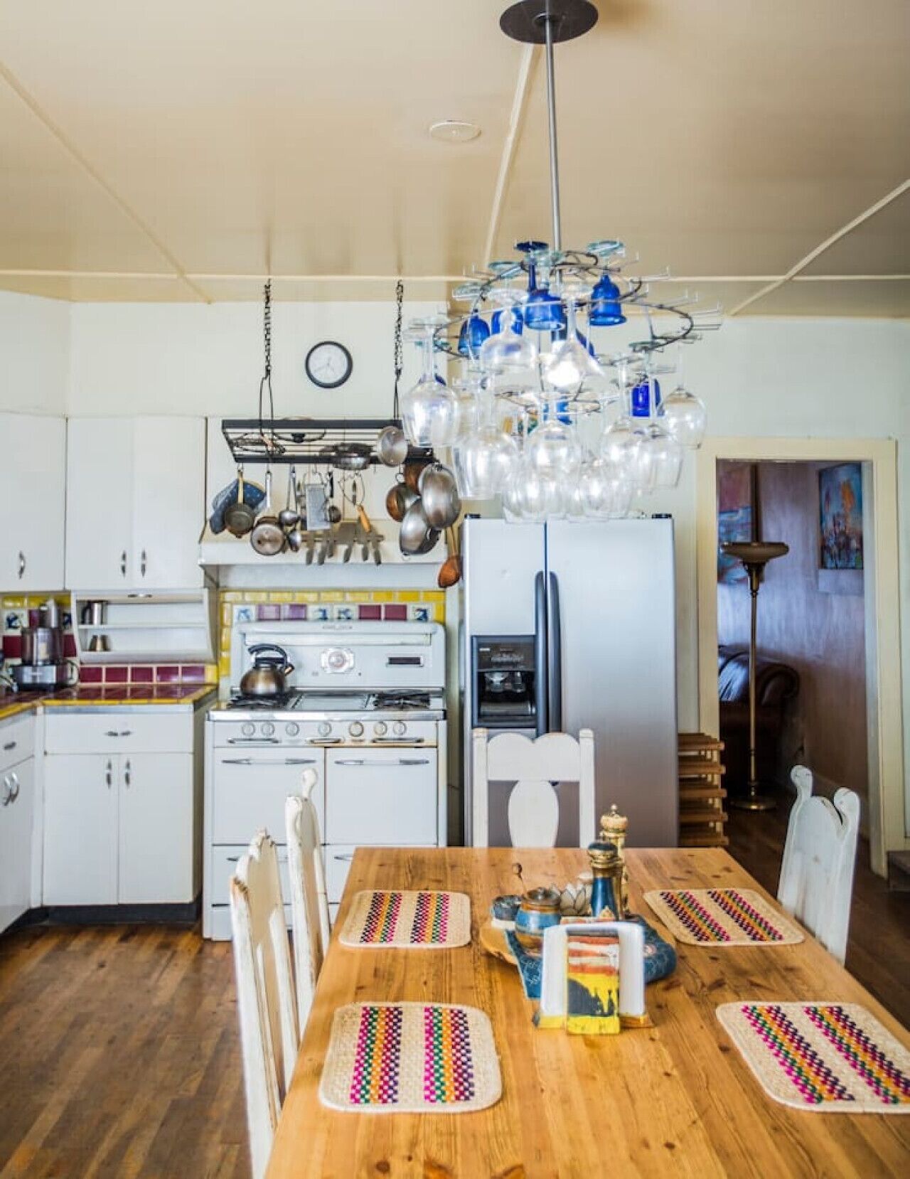A kitchen with white cabinets, a stove, oven, and a refrigerator. There is a dining table with chairs and a chandelier above.