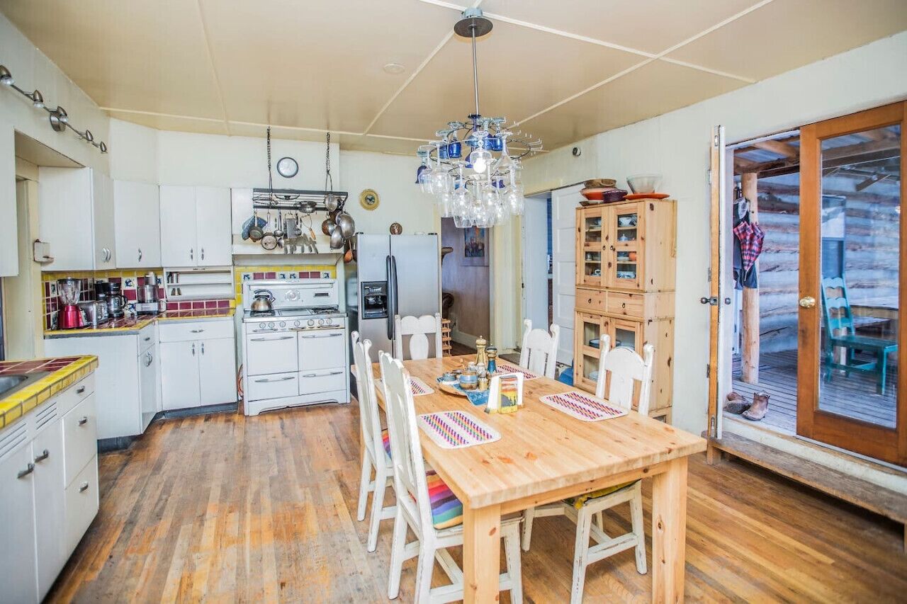 Une cuisine avec des meubles blancs, une table à manger en bois et un luminaire suspendu.