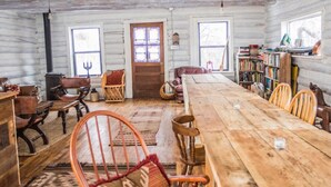 Ein rustikales Blockhaus-Interieur mit einem langen Esstisch, Ledersesseln, einem Kamin und einem Bücherregal.