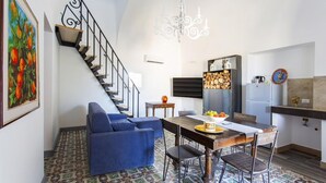 A compact living space with a staircase, a dining area with a wooden table and chairs, a sofa, a chandelier, and a kitchen area with a refrigerator and a cabinet. - Rustic Sicilian hamlet area Partinico / Alcamo/ Balestrate (Partinico)