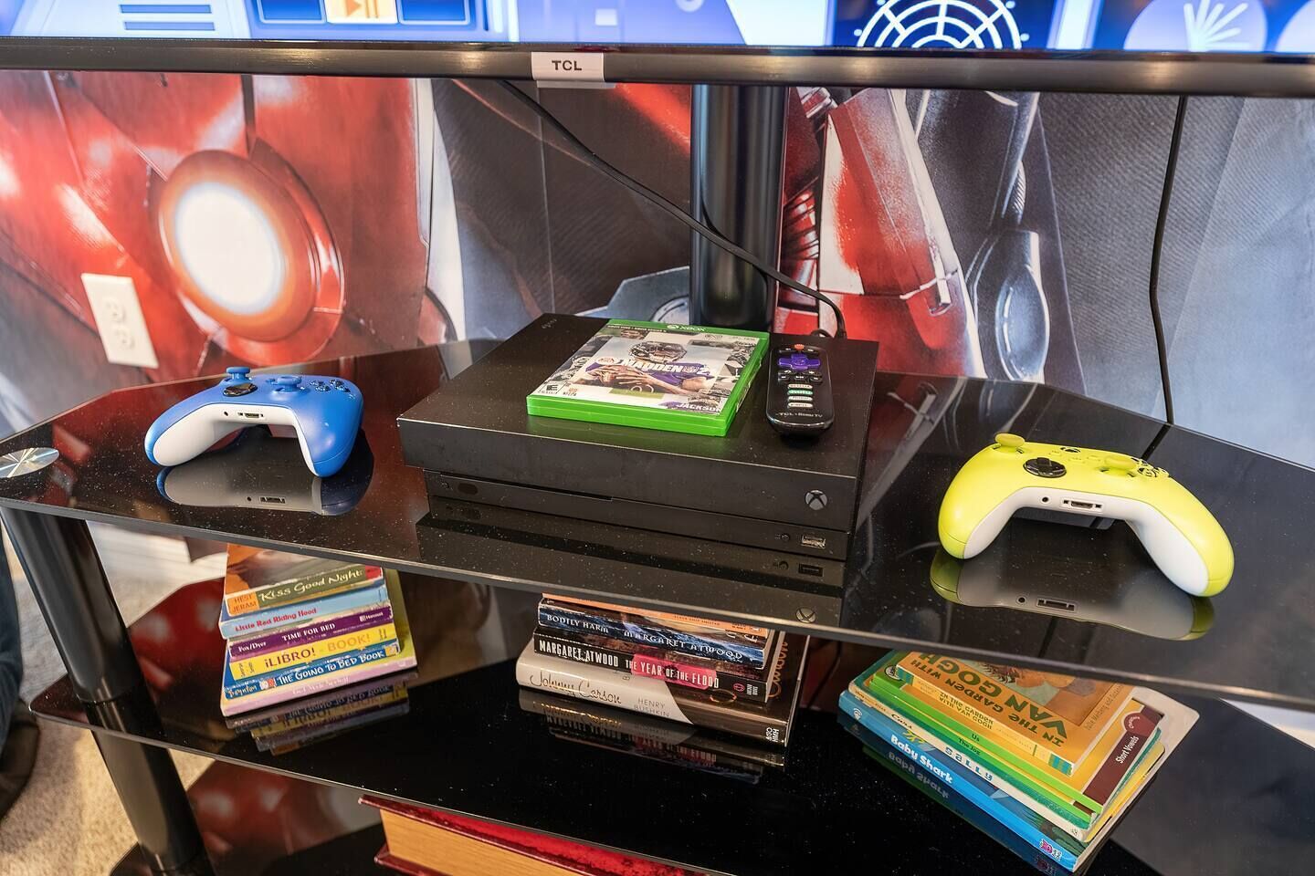 A glass display case with video game controllers, a green game box, and a stack of books.