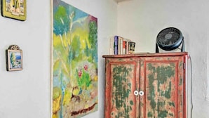 Una habitación con un cuadro abstracto grande, un aparador rojo con libros y un ventilador.