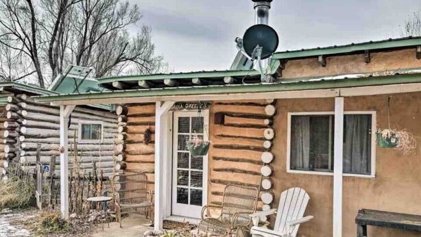 Una cabaña de troncos con un porche, chimenea y mobiliario para exterior.