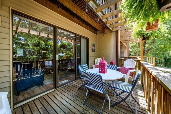 A covered patio with a wooden deck, outdoor seating, and a view of the surrounding greenery.