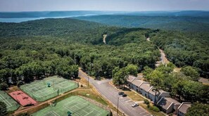 Vue aérienne d’un quartier résidentiel avec des courts de tennis, une route et un paysage boisé.