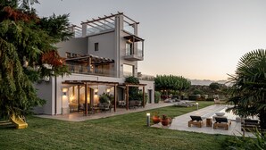 A modern two-story house with a balcony, outdoor seating area, and a well-maintained lawn. - Villa Heora - The Floating Residence (Tria Monastiria)